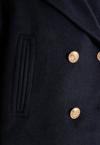 Manteau en laine navy avec un design à double boutonnage, des boutons ornés d'ancres dorées, et une poche latérale avec des détails de couture verticale.