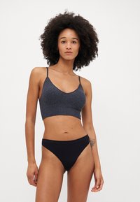 Tamsiai pilka kirpta bralette su plonais petnešomis, turinti tekstūruotą raštą. Juodos spalvos aukšto liemens bikini apatinė dalis su lygia apdaila.