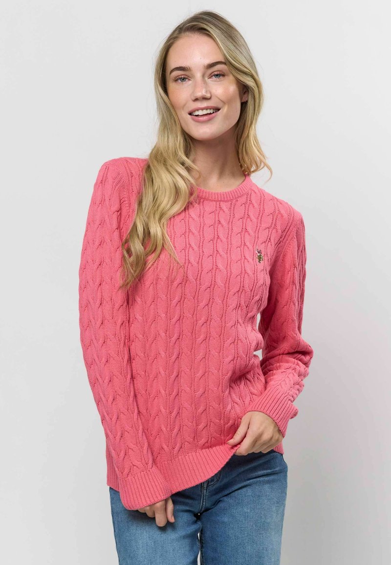 Lyserød kabelstrikket sweater med ribbestrikkede manchetter og kant. Har et lille logo på brystet. Blød tekstur, lange ærmer og rund halsudskæring.