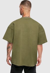 Olivově zelené oversized tričko vyrobené z bavlny, se vzhledem kulatého výstřihu a krátkými rukávy, viditelnými švy a uvolněným střihem.