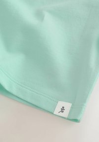 Camiseta verde menta con una textura suave, que incluye una etiqueta blanca simple con un pequeño gráfico. Dobladillo y acabado del borde cuidadosamente cosidos.