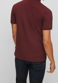 Burgundy pikétröja med korta ärmar, med ribbad krage och muddar, i kombination med mörk denimjeans. Enkel design, inga synliga mönster.