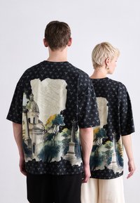 Sorte kortærmede t-shirts med et detaljeret landskabsprint på ryggen, med bløde teksturer og subtile farver som grøn og beige.
