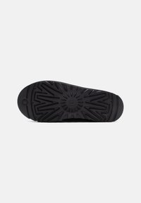 Semelle de chaussure en caoutchouc noir avec un motif texturé, présentant des rainures profondes et un design circulaire au centre pour assurer une adhérence.