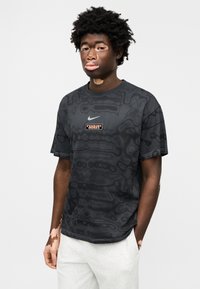 Μαύρο μπλουζάκι με υφασμένο σχέδιο, με λογότυπο Nike στο στήθος και στρογγυλή λαιμόκοψη. Φορεμένο με ανοιχτό γκρι φόρμα.