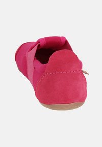Pink suede slip-on shoe featuring a rounded toe, flexible sole, and a textured fabric upper. Heel includes a soft fabric loop for easy wearing.