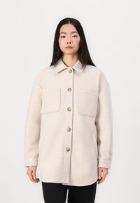 Beige Wollmischung Hemdjacke mit Kragen, zwei Fronttaschen und großen Knöpfen. Lockere Passform mit langen Ärmeln und einer glatten Textur.