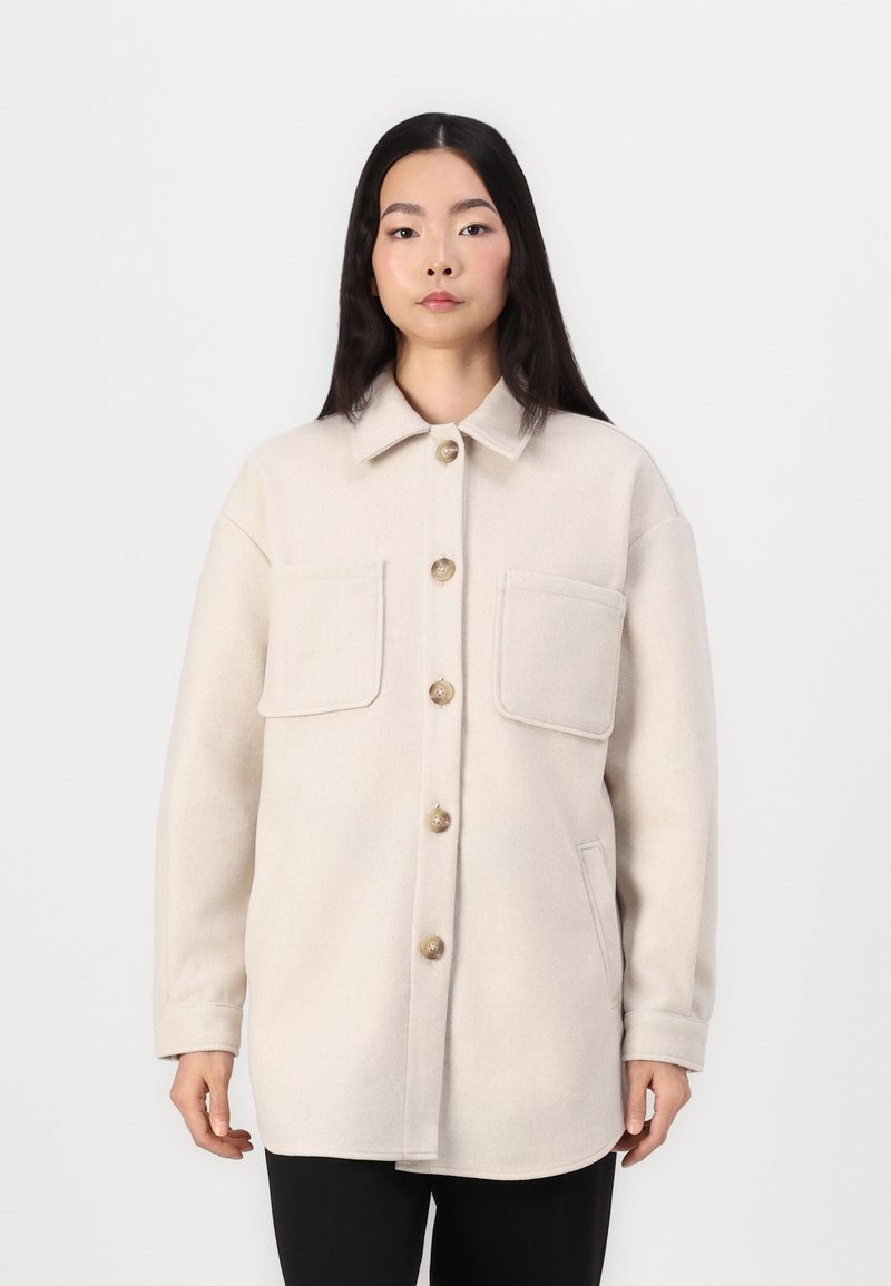 Beige wool blend shirt jacket with a collar, two front pockets, and large buttons. Relaxed fit with long sleeves and a smooth texture.