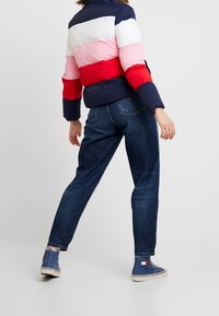 Padded jacket with horizontal stripes in navy, white, pink, and red, paired with dark blue jeans and blue high-top sneakers.