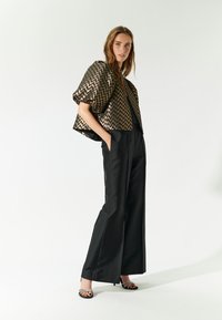 Giacca corta a zigzag in metallo nero e oro abbinata a pantaloni neri a gamba larga con vita alta e sandali neri con tacco e cinturini.