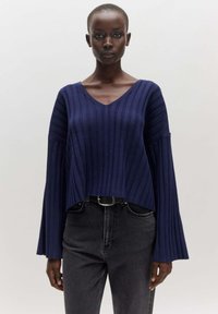 Marineblauer, gerippter Strickpullover mit V-Ausschnitt, weiten Glockenärmeln und cropped Saum, kombiniert mit hochgeschnittenen schwarzen Jeans.