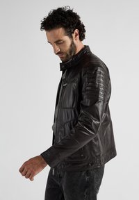 Svart läderjacka med kviltade axelpartier, dragkedjefickor och hög krage. Slät textur och skräddarsydd passform.