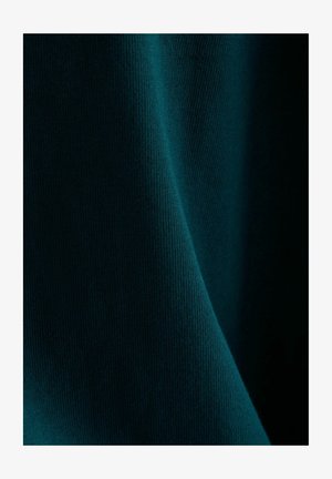 Tessuto verde petrolio scuro con texture a coste sottili, morbido piegato creando ombre delicate e riflessi.