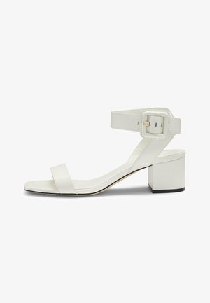 White leather heeled sandals featuring a thin strap across the toes, an ankle strap with a square buckle, and a block heel.