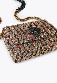 Borsa intrecciata in tessuto multicolore con tracolla in catena nera e dorata. Presenta un accento di un uccello nero e lettere in rilievo che spellano "KURT."