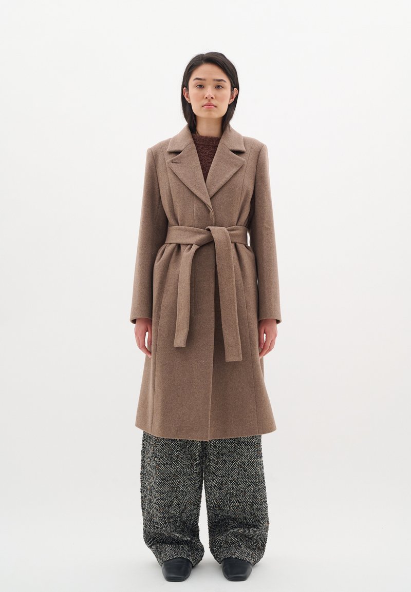 Cappotto in misto lana marrone con vita vita regolabile, grandi rever e maniche lunghe, abbinato a pantaloni a gamba larga in motivo houndstooth.