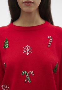 Rode sweater met met pailletten versieringen van kerstbomen, sneeuwvlokken en zuurstokken in groen, zilver en rood. Zachte textuur en ronde hals.
