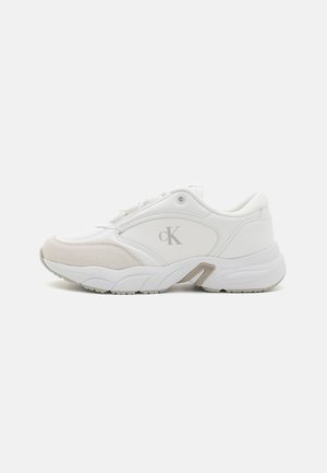 Biały niski sneaker z beżowym zamszowym noskiem, szare logo "cK" po boku, gruba podeszwa i sznurowane zapięcie na jednolitym tle.