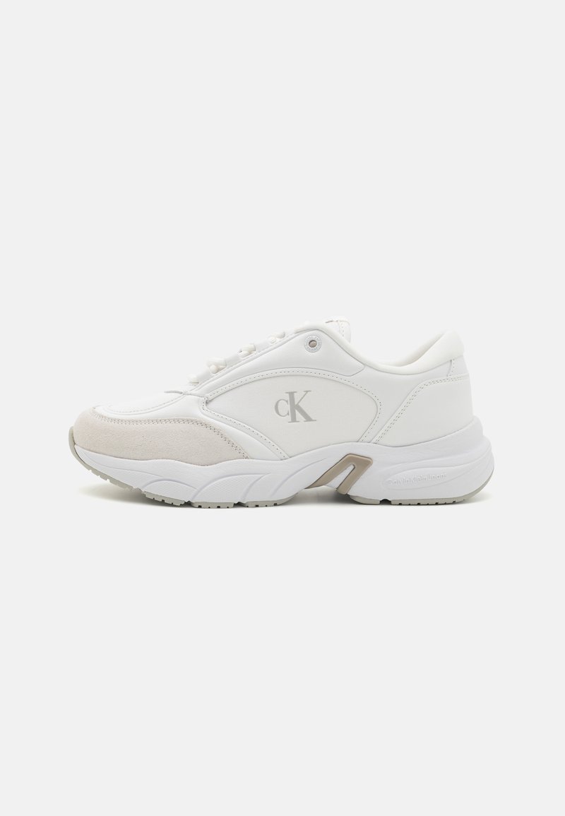 Basket blanche basse avec bout en daim beige, logo gris "cK" sur le côté, semelle épaisse et fermeture lacets sur fond uni.