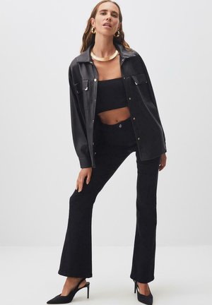 Black faux leather jacket with snap buttons, paired with a black crop top and flared pants. Accented by metallic jewelry and black heels.