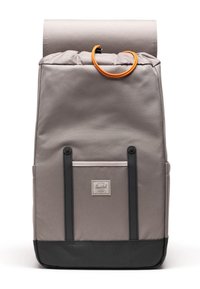 Mochila rectangular de tela gris con base negra, bolsillo frontal, dos correas verticales negras y cordón de cierre naranja en la solapa superior.