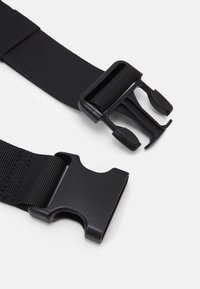 Svart plastspänne med sidfrigöring och justerbar svart nylonrem på en vit bakgrund, öppnad.