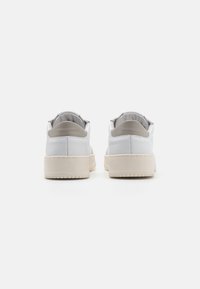 White leather sneakers with beige accents, padded collars, low-profile design, textured soles, and contrasting stitching.