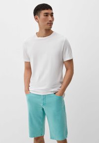 Biała koszulka z krótkim rękawem zestawiona z jasno turkusowymi szortami do kolan, posiadającymi boczne kieszenie i luźny krój. Miękka w dotyku.