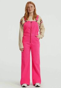Bright pink corduroy overalls with a front zipper, wide legs, and adjustable shoulder straps. Paired with a beige long-sleeve top.