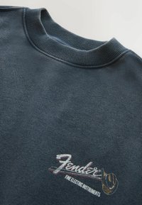 Tmavosivá mikina s textúrovaným rebrovaným golierom a logom "Fender Fine Electric Instruments" s grafikou kovbojského klobúka na hrudi.