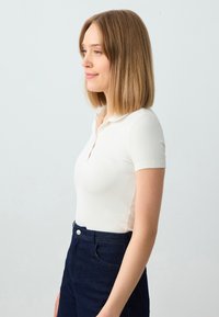Witte geribde polo shirt met een korte kraag, gecombineerd met donkerdenim hoge taille broek met een knoopsluiting aan de voorkant en zakken.