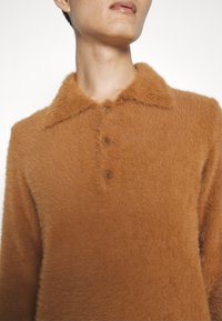 Brun krage tröja gjord av fluffigt material, med tre knappar och en texturerad yta. Närbild som framhäver kragen och tyget.