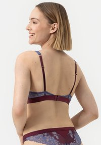 Krajková podprsenka s hlubokým burgundským základem a světle fialkovým krajkovým lemem. Na zadní straně jsou viditelné nastavitelné pásky a zapínání na háček.