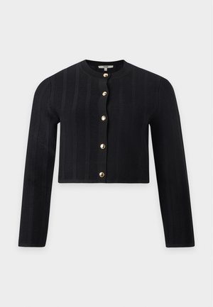 Femme portant un blazer beige à fines rayures avec des boutons dorés, un short assorti longueur genoux, un haut noir boutonné, une ceinture chaîne et des talons hauts beiges.