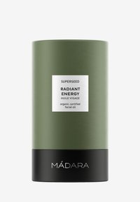 Grön cylindrisk behållare med matt yta, svart botten och vit etikett. Texten inkluderar "SUPERSEED," "RADIANT ENERGY," och "ekologiskt certifierad ansiktsolja."