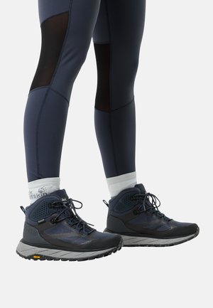Marineblau Wanderschuhe aus Mesh und synthetischem Überzug, mit strukturierten Sohlen, schwarzen Akzenten und reflektierenden Details. Getragen mit figurbetonten marineblauen Leggings.