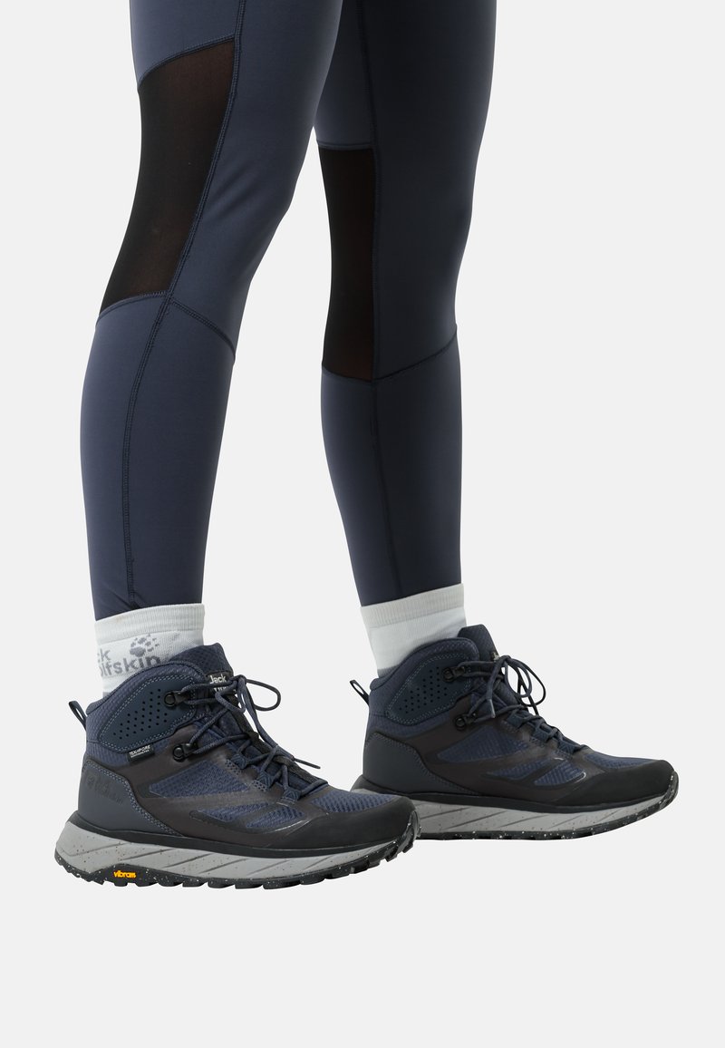 Marineblau Wanderschuhe aus Mesh und synthetischem Überzug, mit strukturierten Sohlen, schwarzen Akzenten und reflektierenden Details. Getragen mit figurbetonten marineblauen Leggings.
