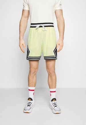 Fel limoengroen sportbroekje van mesh met zwarte accenten, een elastische tailleband en een trekkoord. Gecombineerd met wit-rood gestreepte sokken en sneakers.