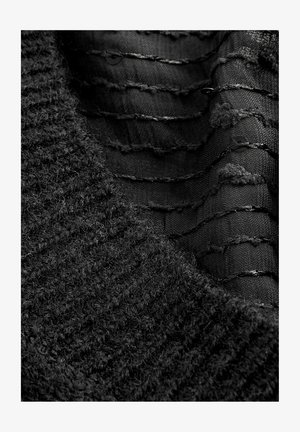 Black fabric layered design featuring textured knit and smooth woven sections with horizontal stitching and small round accents.