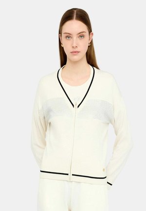 Cardigan crema con zip, dettagli neri, pannello frontale testurizzato, maniche lunghe e scollo a V. Presenta un logo dorato all'orlo.