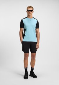 Light blue short-sleeve athletic shirt with black accents, paired with black shorts and black sneakers. Features a logo on the shirt.
