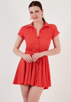 Short-sleeve, coral dress with a button-up design, a fitted waist, and a flared skirt; made of textured fabric with a tie at the waist.