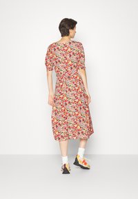 Vestido midi floral em vermelho, rosa e amarelo com mangas curtas bufantes, cintura ajustada e um tecido suave; combinado com ténis coloridos.