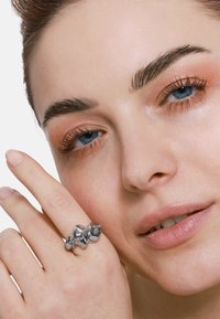Anello in argento con un design fluido e organico, caratterizzato da una texture metallica lucida. Vista ravvicinata di una mano che accarezza delicatamente l'anello.