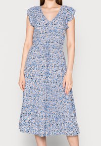 Blumenkleid mit blauem Hintergrund, ausgestattet mit kurzen Rüschensäumen, einem V-Ausschnitt und einem Bindegürtel. Der Stoff hat einen gerafften Rock und ein mehrfarbiges Blumenmuster.