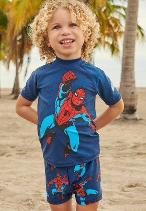 Tamsiai mėlynos spalvos vaikų maudymosi kostiumėlis, kuriame vyrauja raudona ir šviesiai mėlyna spalva su „Spider-Man“ grafika, trumpomis rankovėmis viršus ir atitinkamos šortai su panašiu dizainu.