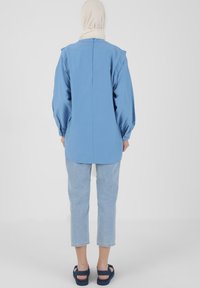 Tunic blu con maniche lunghe, taglio dritto e maniche a palloncino, abbinato a jeans cropped in denim chiaro e sandali blu navy. Tessuto morbido.
