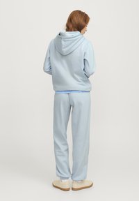Felpa con cappuccio azzurro chiaro dotata di coulisse e pantaloni jogger abbinati, realizzati in tessuto morbido; vestibilità comoda con polsini e vita a costine.
