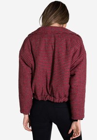 Chaqueta acolchada a cuadros rojos y negros con hombros caídos, dobladillo elástico y un acabado de tela texturizada. Presenta un escote redondo y mangas largas.