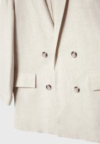 Blazer beige clair croisé avec quatre boutons et deux poches avant à rabat, fabriqué en tissu texturé.